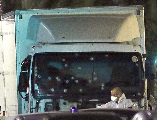 A forensic officer stands near a van with its windscreen riddled with bullets, that plowed through a crowd of revelers who'd gathered to watch the fireworks in the French resort city of Nice, southern France, Friday, July 15, 2016. At least 80 people were killed before police killed the driver, authorities said. (AP Photo/Claude Paris)